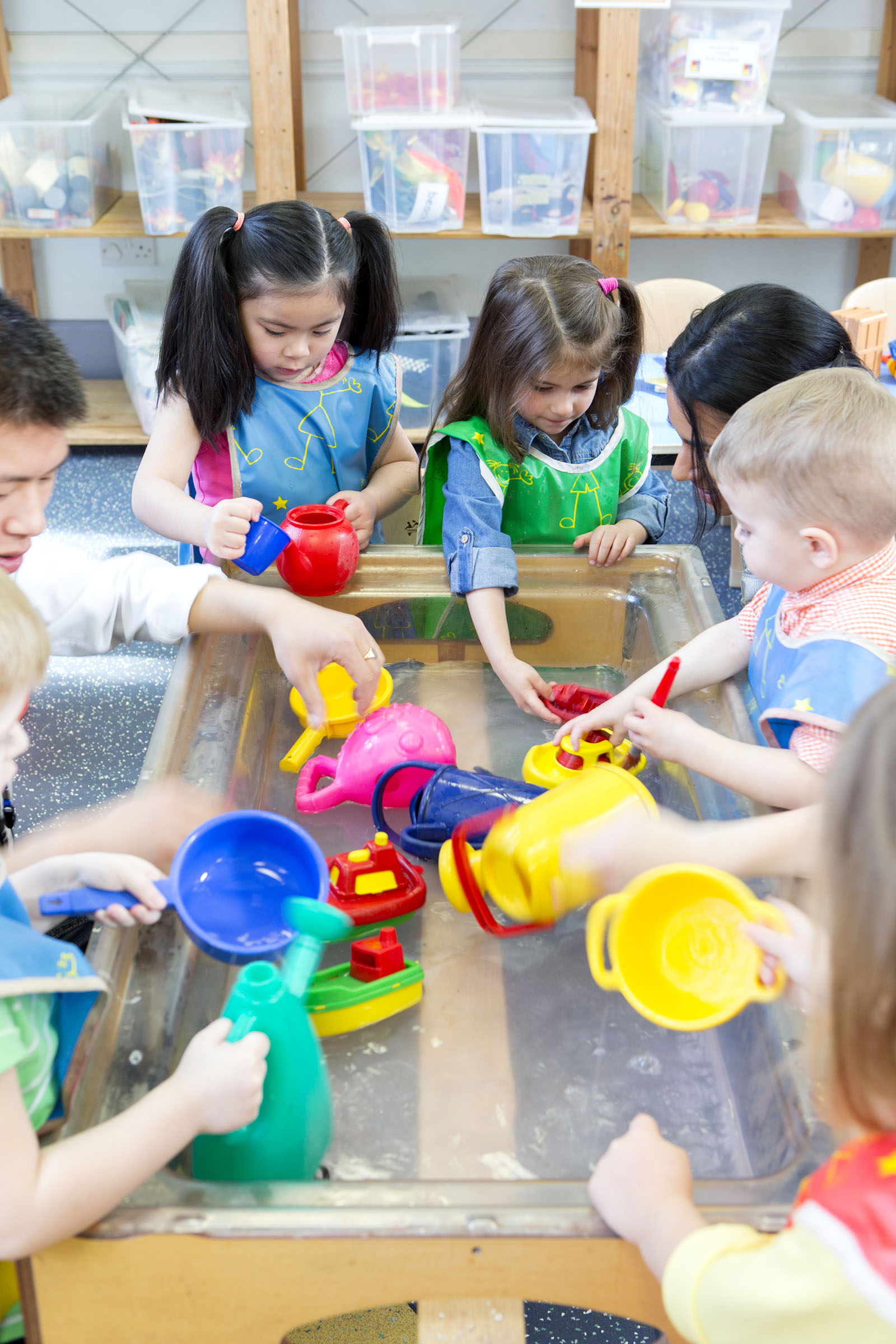 Group of nursery children playing at a water table with their teacher.